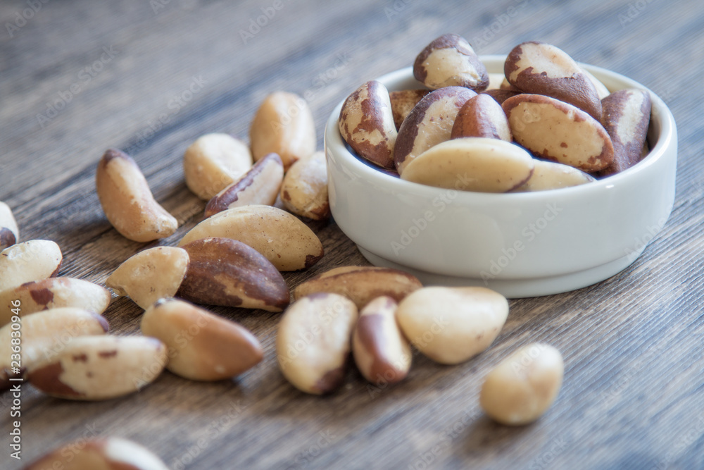 White bowl with Brazil nuts and wooden background. White bowl with Brazil nuts and wooden background.