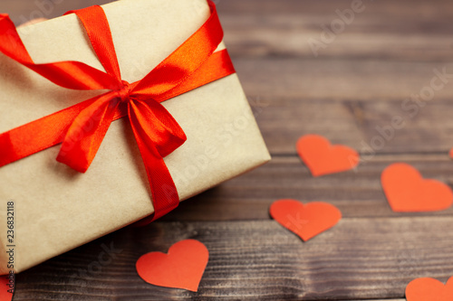 Gift box with red ribbon and heart on wooden background