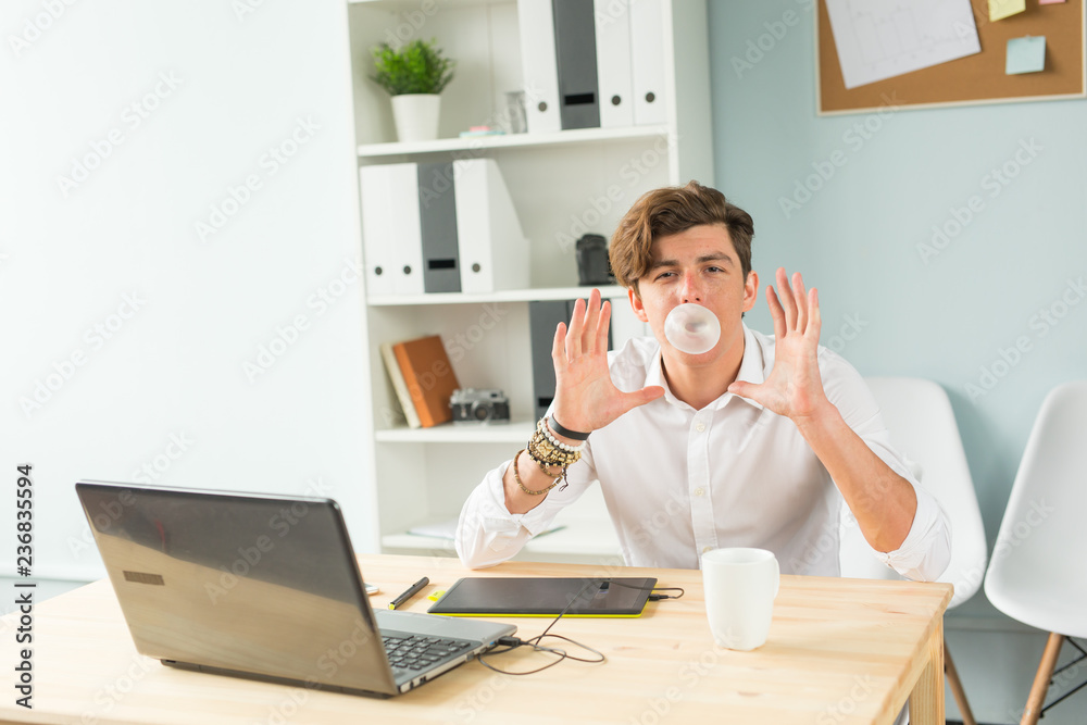 Business, fun and joke concept - young man blowing bubble of chewing gum in office
