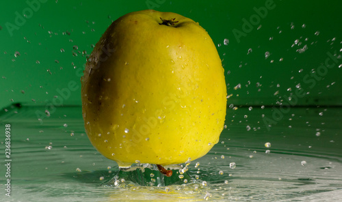 Green apple and splashes of water on a colored background