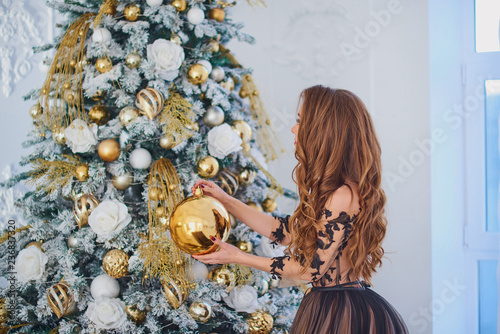 Young beautiful woman with long hair in a dress with a train decorates the Christmas tree