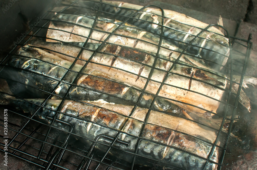 Mackerel fish grilled on iron plate in rural house fireplace closeup with white smoke