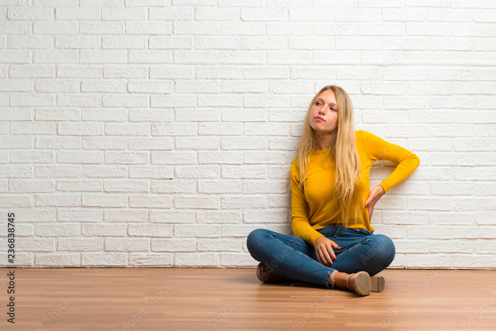 Young girl sitting on the floor suffering from backache for having made an effort Young girl sitting on the floor suffering from backache for having made an effort