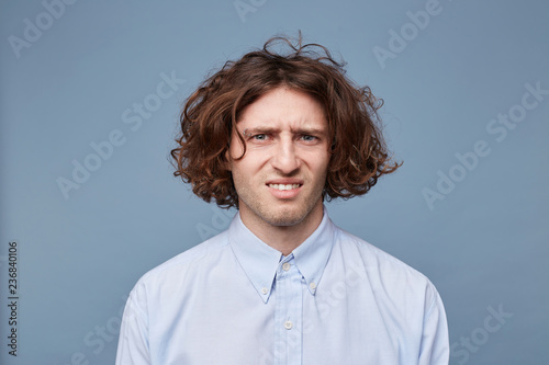 Картината върху платно The guy with an untidy messy hairstyle looks camera, dressed in an ordinary light shirt, a facial expression of disgust displeasure dislike