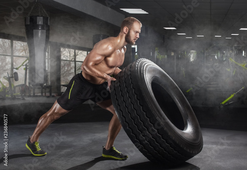 Young adult man flipping and rolling tire during exercise in the gym. Sports concept, fat burning and a healthy lifestyle.