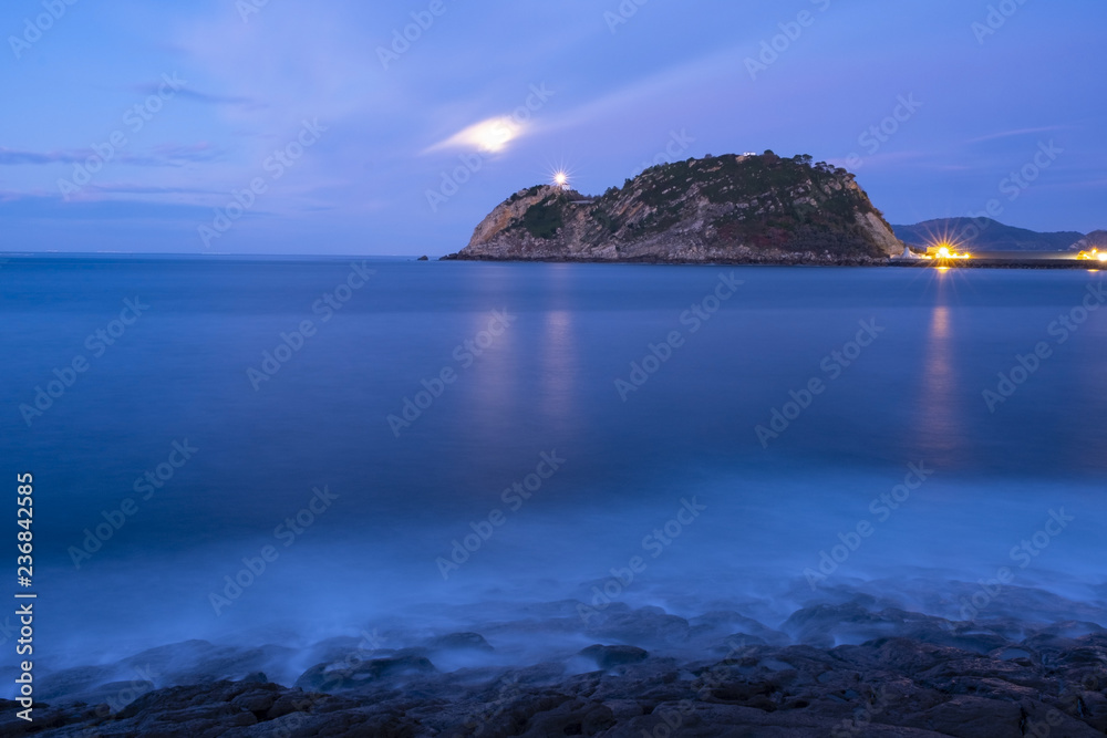 light of Getaria lighthouse and fullmoon over the sea at night, Euskadi