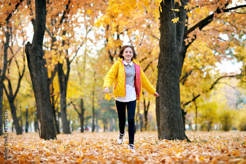 Happy teen girl is running in autumn park with big maple's leaf. Bright yellow leaves and trees. © soleg