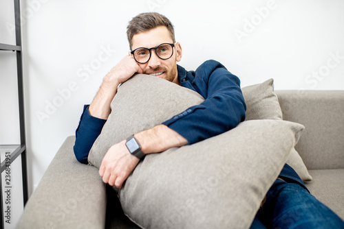Cute man dressed casually relaxing on the couch with a pillow while watching TV at home