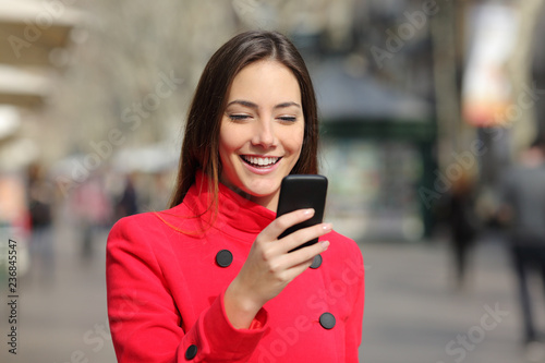 Happy woman walks using phone in winter in the street
