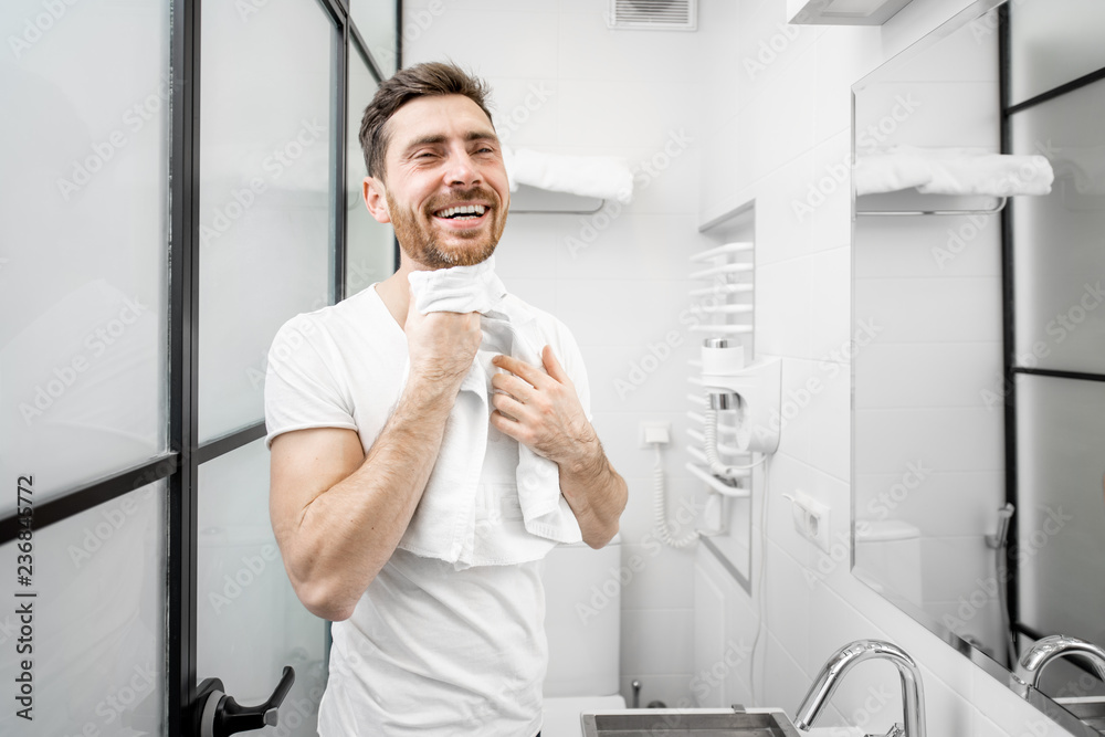 Portrait of a handsome man in white t-shirt drying his face with towel in the bathroom