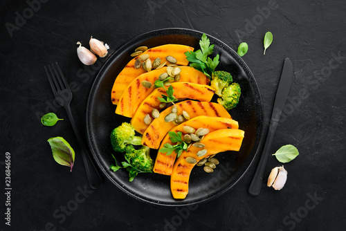 Baked pumpkin with pumpkin seeds and broccoli. On a black background. Top view. Free space for your text.