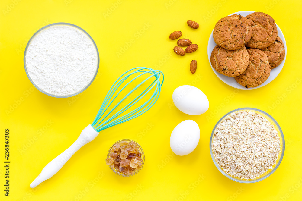 Cook cookies at home concept. Ingredients and instruments for make cookies. Fresh cookies near flour, eggs and whisk on yellow background top view Cook cookies at home concept. Ingredients and instruments for make cookies. Fresh cookies near flour, eggs and whisk on yellow background top view
