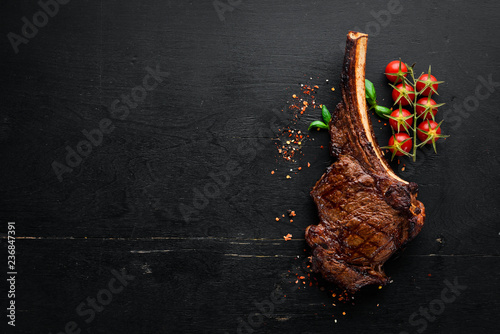 Steak on the bone. tomahawk steak On a black wooden background. Top view. Free copy space. photo