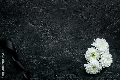 Funeral symbols. White flower near black ribbon on black background top view copy space