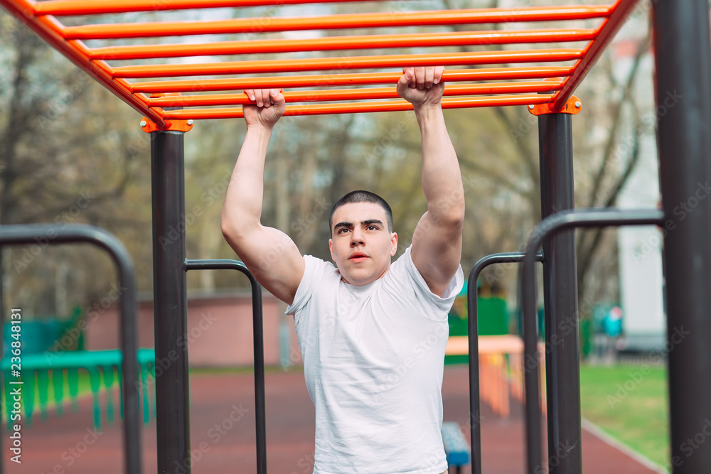 Fit man cross training on monkey bars . Fitness workout on brachiation ladder in an outdoor gym outside.