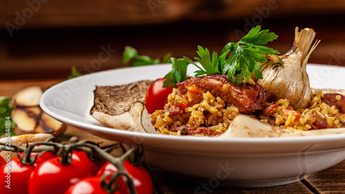 The concept of Eastern, Turkish, Uzbek cuisine. Pilaf with pieces of meat is served in pita bread, in a white plate on a wooden table. parsley and vegetables on the table.