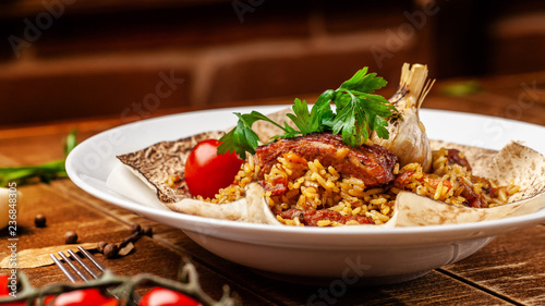 The concept of Eastern, Turkish, Uzbek cuisine. Pilaf with pieces of meat is served in pita bread, in a white plate on a wooden table. parsley and vegetables on the table.