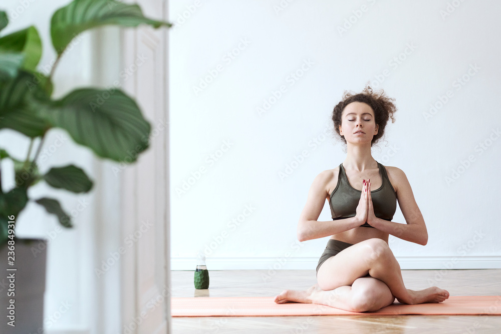 Young active, dark hair woman exercising and stratching her body on the floor at her studio. Girl is practicing yoga and thinking about positive things. Healthy lifestyle and mental balance. 