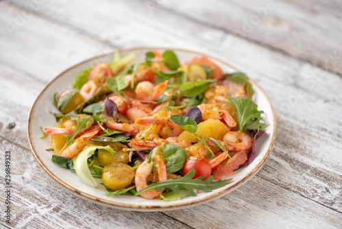 salad with shrimps and assorted salads (arugula, cherry tomatoes, chard, spinach) on white wooden background