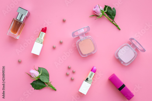 Rose tone cosmetics. Lipstick, bulk, eyeshadow among rose flowers on pink background top view