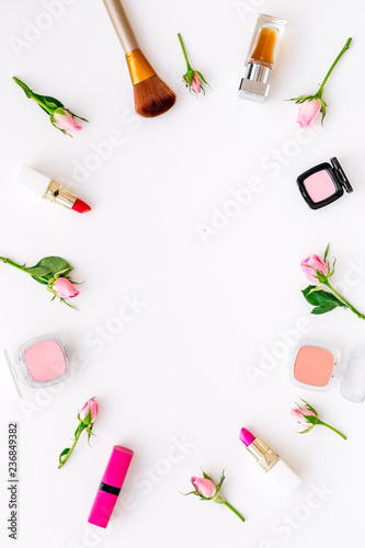 Rose, pink decorative cosmetics frame. Lipstick, bulk, eyeshadow and small rose flowers on white background top view copy space