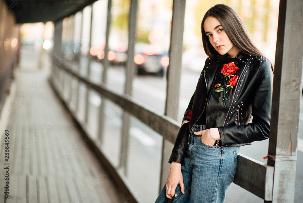 Portrait young punk rock fashion girl in a black leather jacket with stilettos in an urban environment of a street warehouse, woman in jeans walking