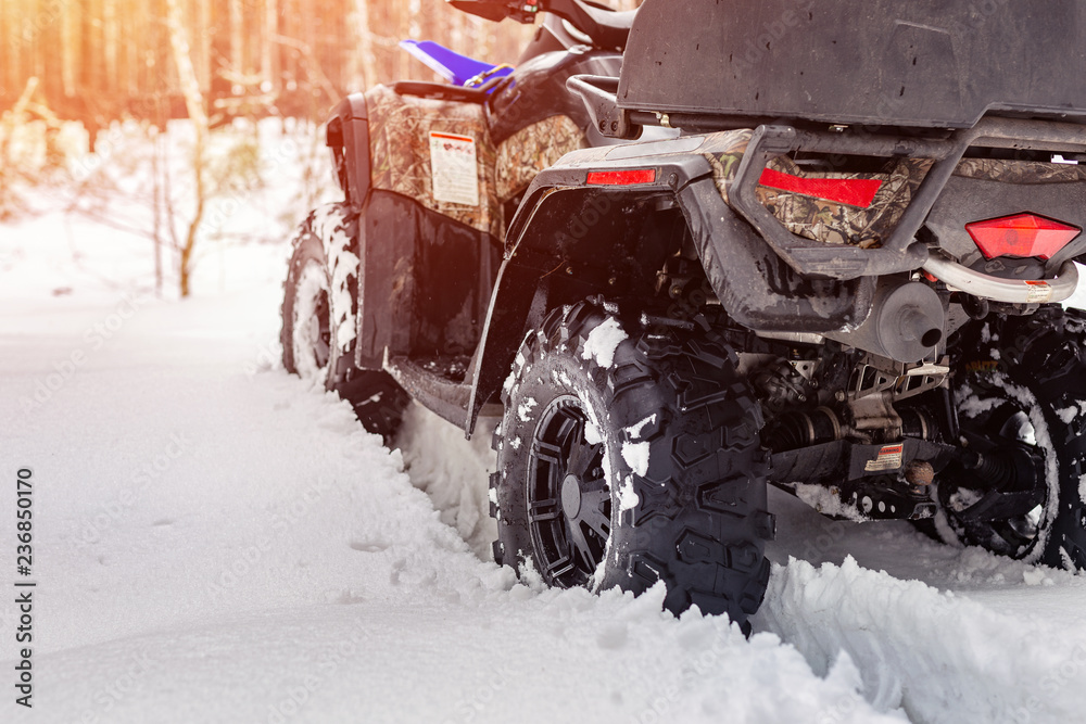 Obraz premium Close-up ATV 4wd quad bike in forest at winter. 4wd all-terreain vehicle stand in heavy snow with deep wheel track. Seasonal extreme sport adventure and trip. Copyspace
