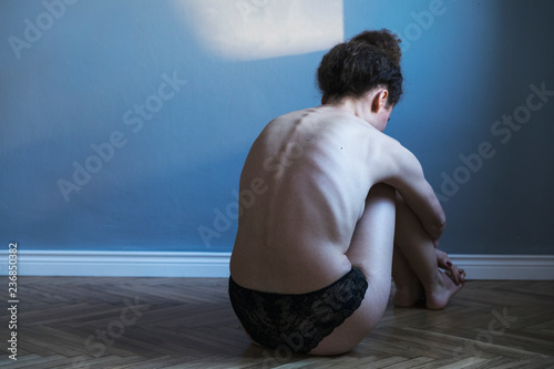 Foto Young woman with anorexia and depression sitting alone on the flor in gray room