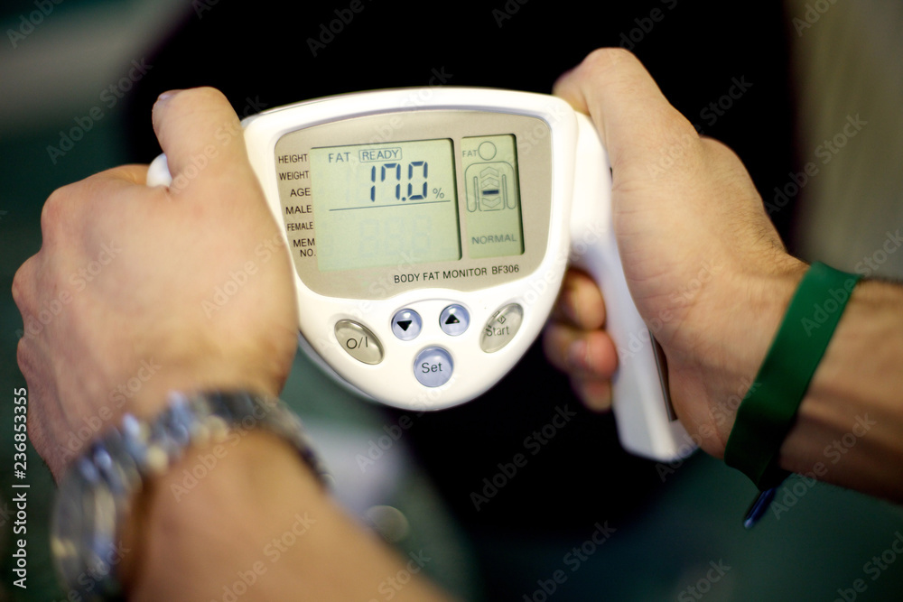 close of a mans hands using a body fat monitor with a 17 percent fat rating close of a mans hands using a body fat monitor with a 17 percent fat rating