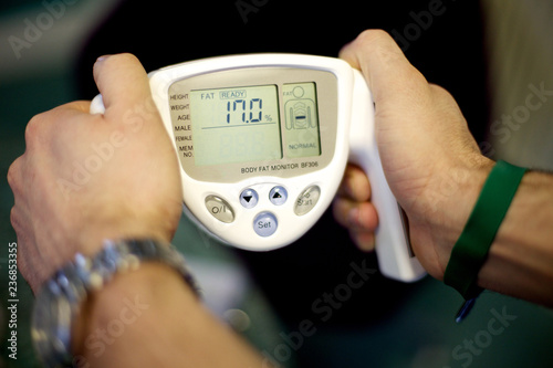 close of a mans hands using a body fat monitor with a 17 percent fat rating