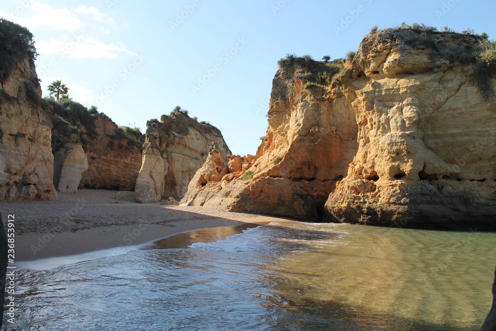 Beautiful view of a sunny beach with crystal clear blue water and fine white sand next to a steep rocky cliff in Lagos, Algarve, Portugal