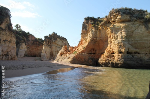 Beautiful view of a sunny beach with crystal clear blue water and fine white sand next to a steep rocky cliff in Lagos, Algarve, Portugal © duqimages