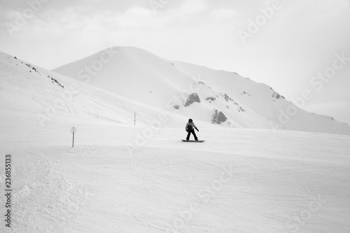 Snowboarder downhill on snowy ski slope and mountains in fog