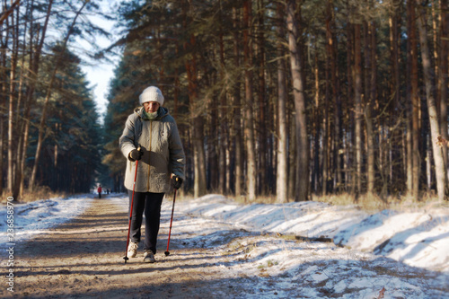 Active senior lady engaged in Nordic walking with sticks in the winter forest