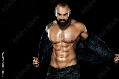 Men fashion concept. Close-up portrait of a brutal bearded man topless in a leather jacket. Athlete bodybuilder on black background.