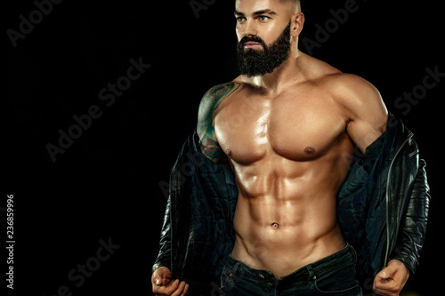 Men fashion concept. Close-up portrait of a brutal bearded man topless in a leather jacket. Athlete bodybuilder on black background. © Mike Orlov