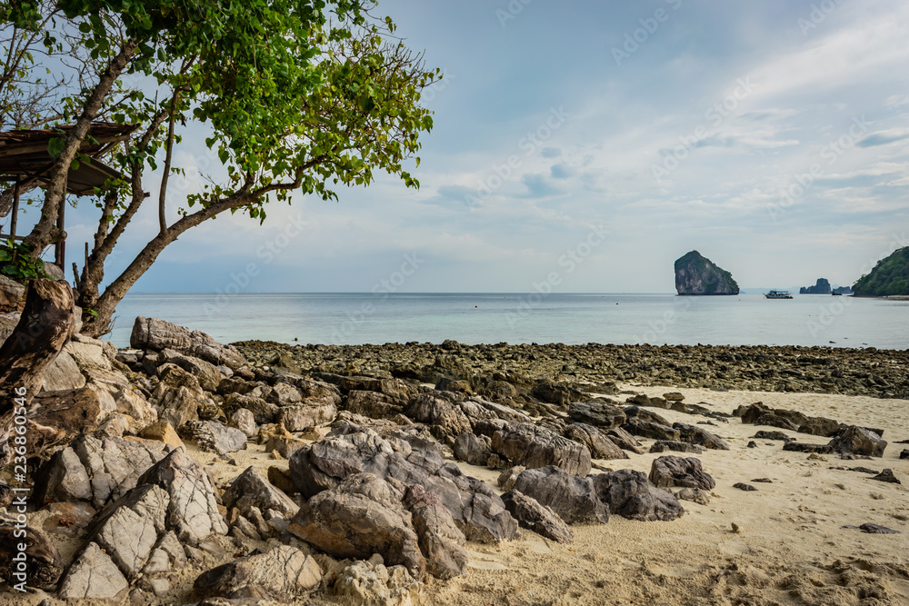 Beach with sand and stones in Krabi area, tree with green leaves on the left, Thai island in the background, small ship, blue sky and sea, Thailand
Beach with sand and stones in Krabi area, tree with green leaves on the left, Thai island in the background, small ship, blue sky and sea, Thailand