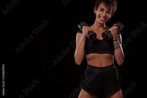 Fitness and sport motivation.. Strong and fit athletic, woman with dumbbells posing on red background in sportswear. © Mike Orlov