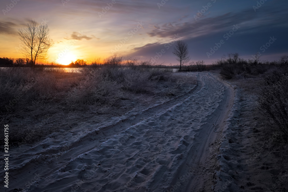 Sand road and trees in the frost, coast of river and sun at sunset. Sand road and trees in the frost, coast of river and sun at sunset.
