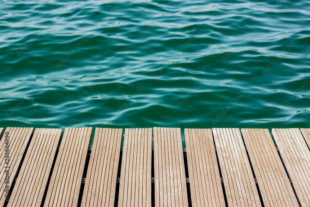 wooden desk waterfront pier floor and fuzzy sea vivid blue and green water background texture, copy space