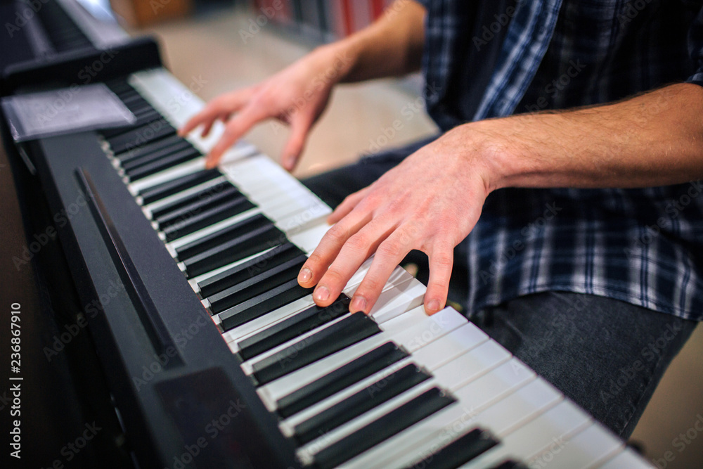 Close up of man playing on keyboard. He sits alone in room.