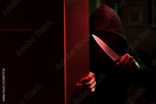 Fotografi Image of killer with knife and in hood in dark apartment with red light