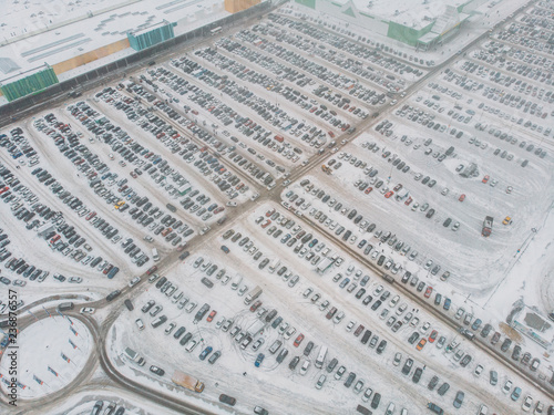 Aerial view of large automobile parking lot with many cars near mall or shopping center in winter with snow, drone photo