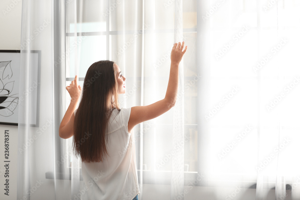 Young woman opening window curtains at home. Space for text Young woman opening window curtains at home. Space for text