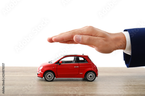 Insurance agent holding hand over toy car on table against white background, closeup
