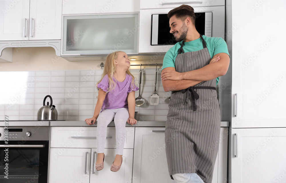 Young man and his daughter in kitchen with modern ovens
