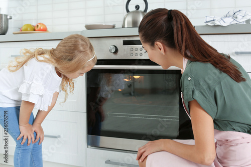 Young woman and her daughter baking something in oven at home