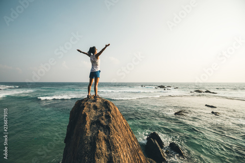 Photo Successful young woman outstretched arms on seaside rock cliff edge