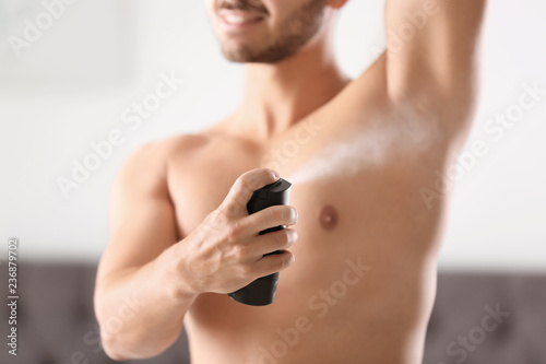 Handsome young man applying deodorant in room