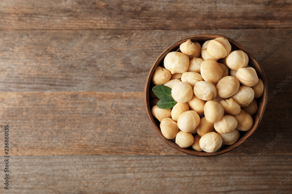 Bowl with shelled organic Macadamia nuts and space for text on wooden background, top view Bowl with shelled organic Macadamia nuts and space for text on wooden background, top view